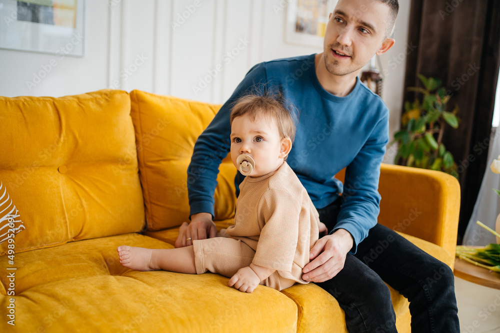 child with a pacifier sitting on a yellow sofa with his father child with a pacifier sitting on a yellow sofa with his father