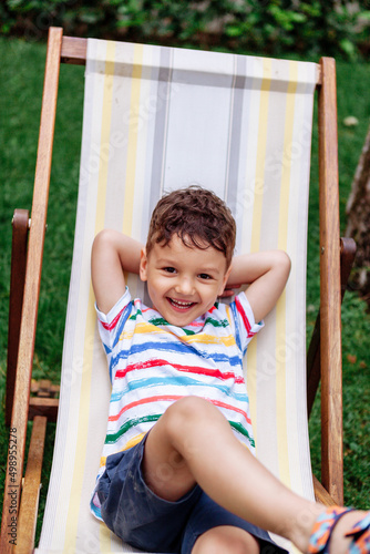 a laughing boy is lying on a folding chair on a chaise longue outside