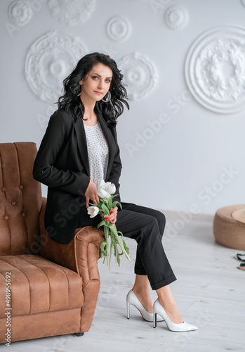Business woman in a black suit sitting on a chair and holding white tulips