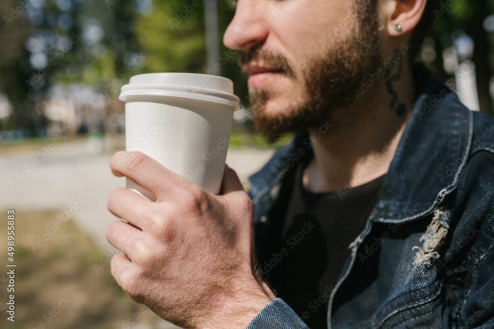 Close up view of young man drinking coffee. He is wearing jean jacket and black sweater. He looks away and thinks. Close up view of young man drinking coffee. He is wearing jean jacket and black sweater. He looks away and thinks.