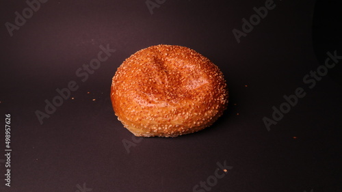 A small bun with sesame seeds for a burger on a black background close up.