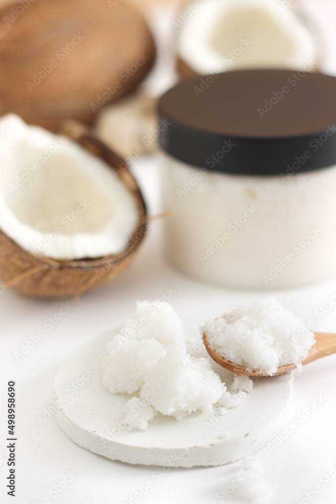 scrub in wood spoon with jar coconut on white background. Home spa treatment concept, organic cosmetic. Vertical photo