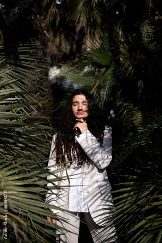 dark-haired brunette in a white business-style suit poses in palm trees. vertical photo