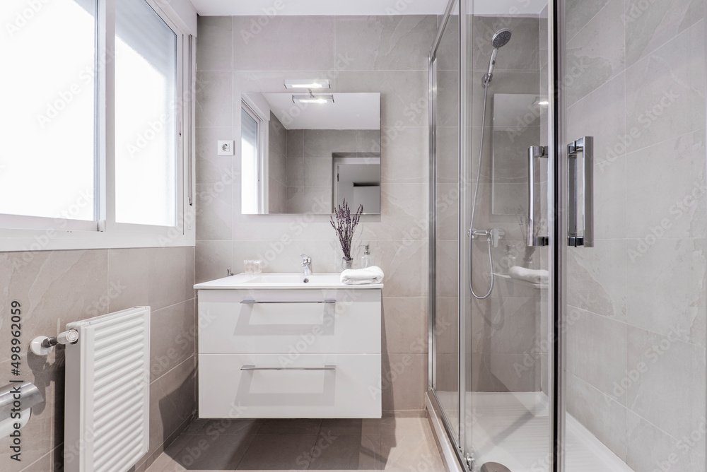 Bathroom with aluminum window, frameless wall mirror, white porcelain sink on white marble top and shower cabin with glass screen and water jets Bathroom with aluminum window, frameless wall mirror, white porcelain sink on white marble top and shower cabin with glass screen and water jets