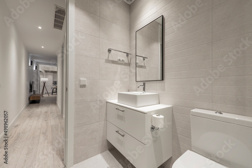 Bathroom with beige paneling and black framed wall mirror  white porcelain sink above vanity next to a hallway