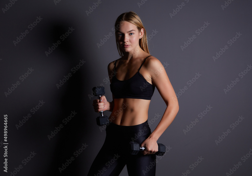 Blonde athletic woman shows her trained body on a dark background. female model trains triceps with dumbbells.