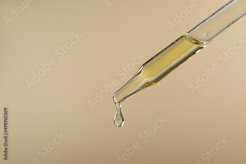 Dripping hydrophilic oil from pipette on beige background, closeup. Space for text