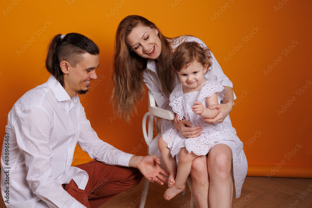 Cute family of father, mother and daughter smiling, playing and joking together. Woman and man kisses and embraces. Happy family with a baby girl on hands kissing daughter Cute family of father, mother and daughter smiling, playing and joking together. Woman and man kisses and embraces. Happy family with a baby girl on hands kissing daughter