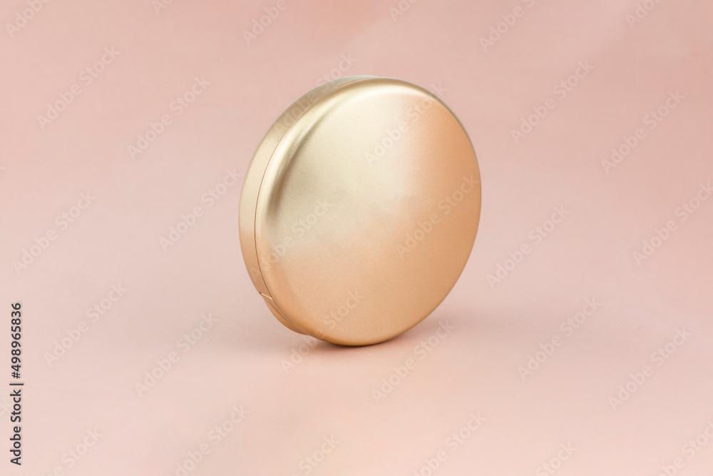 A closed package of face powder on a pink background. Front half-side view. A closed package of face powder on a pink background. Front half-side view.