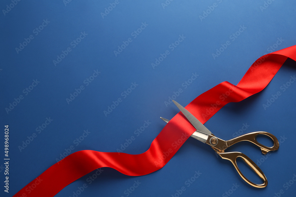 Red ribbon and scissors on blue background, top view. Space for text