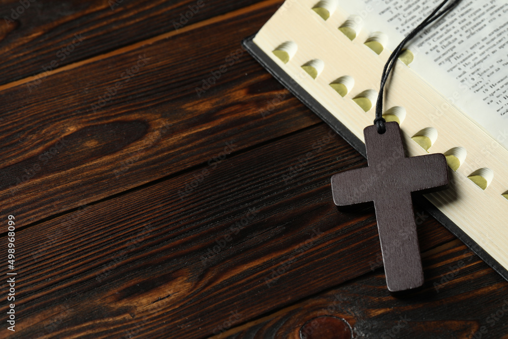 Wooden Christian cross and Bible on table, closeup. Space for text