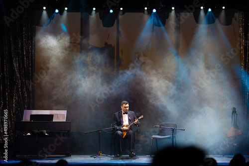 Smoke and light on the stage. Male musicians balalaika player perform a concert on stage