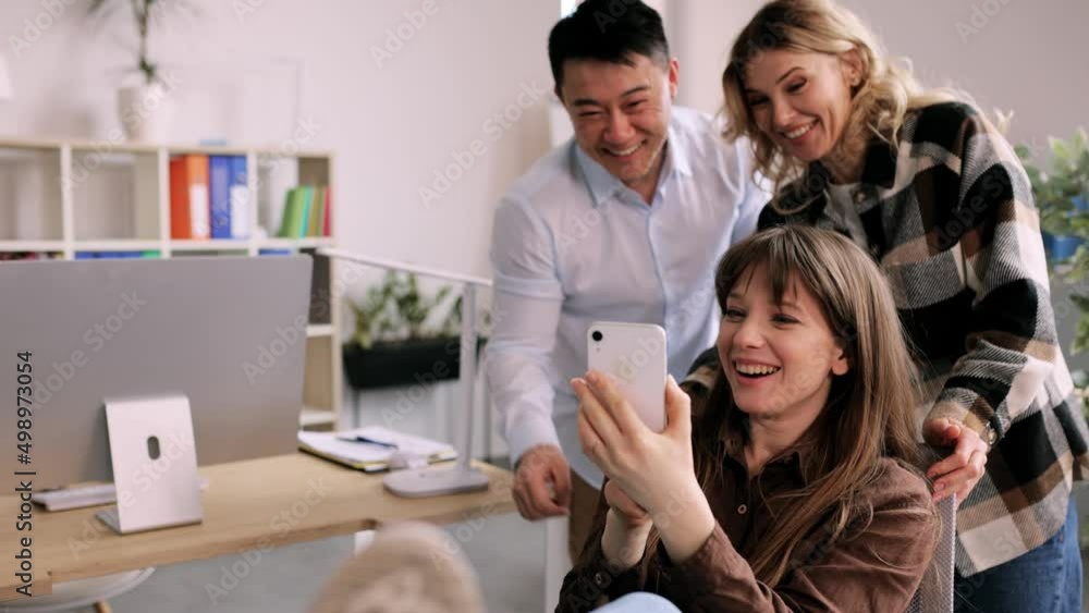 Smiling young woman showing funny videos on smartphone online to happy colleagues. Interracial office workers. High quality 4k footage Smiling young woman showing funny videos on smartphone online to happy colleagues. Interracial office workers. High quality 4k footage