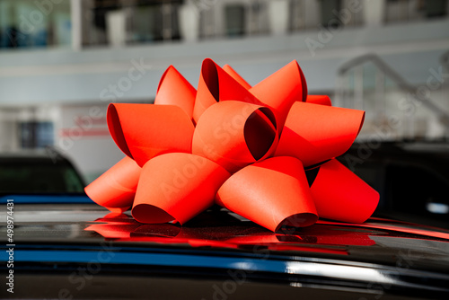 a red gift bow on the roof of a new black car in the car dealership. 
