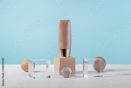 Cosmetic liquid foundation nude cream tube mockup on acrylic and wooden block podium pedestal. Beige concealer base cosmetics product mock up on blue backdrop. Skincare beauty primer, bb corrector