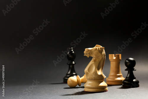 Different chess pieces against dark background, focus on white knight. Space for text photo