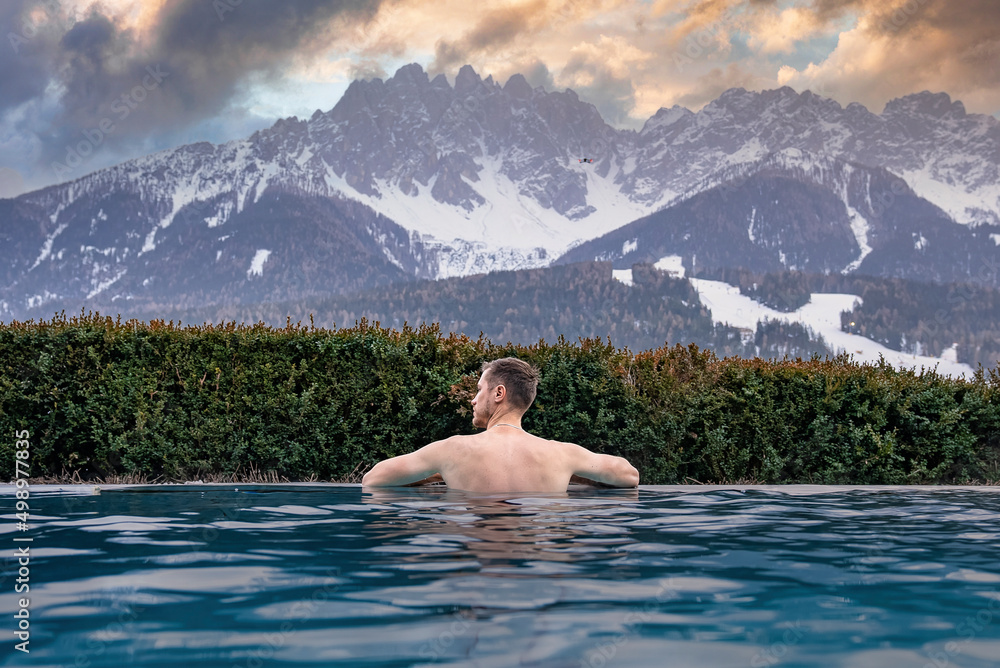 Rear view of man swimming in pool while looking at snowcapped mountain