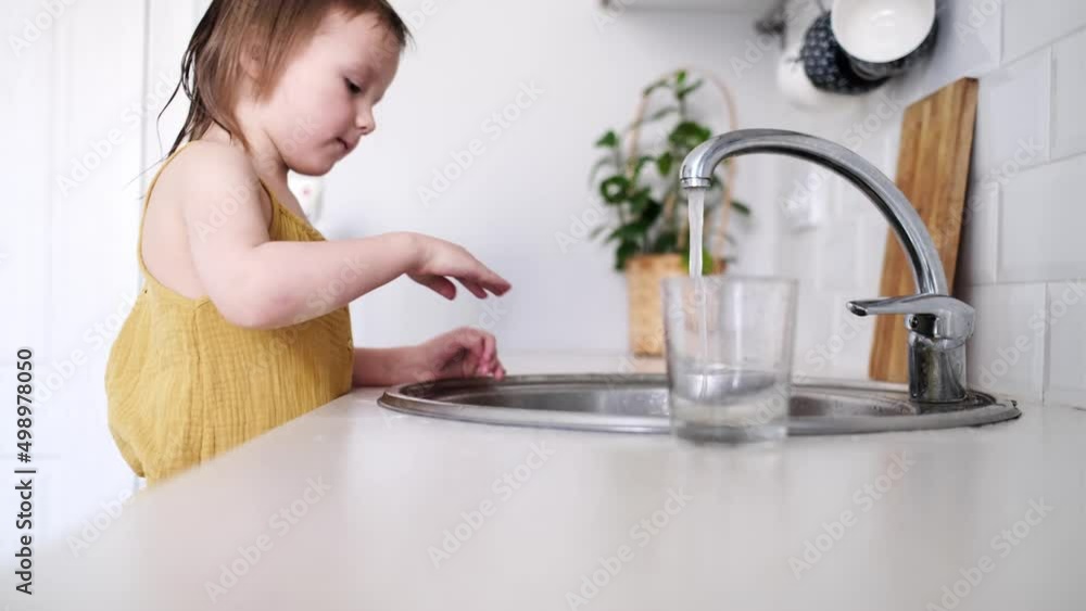 Cute child toddler washes dishes in the sink in the kitchen. Independence of the child and help to the mother. Kid on a stool helps wash dishes, lifestyle in a real interior Cute child toddler washes dishes in the sink in the kitchen. Independence of the child and help to the mother. Kid on a stool helps wash dishes, lifestyle in a real interior