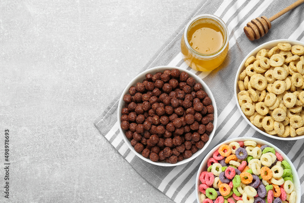 Different delicious breakfast cereals and honey on light grey table, flat lay. Space for text Different delicious breakfast cereals and honey on light grey table, flat lay. Space for text