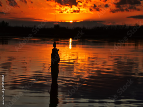 Fishing at sunset. Catching predatory fish on spinning. Sunset colors on the water surface, sunny path from the low sun. Perch caught on yellow spoonbait photo