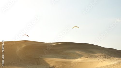 Two paragliders flying over sand dunes in Qatar desert