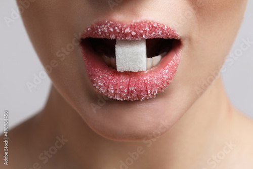 Closeup view of young woman with beautiful lips eating sugar cube on light grey background