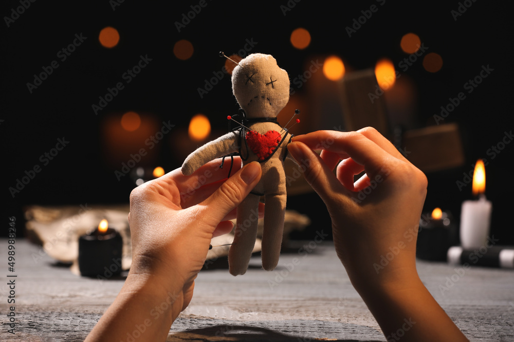 Fototapeta Woman stabbing voodoo doll with pin at wooden table indoors, closeup