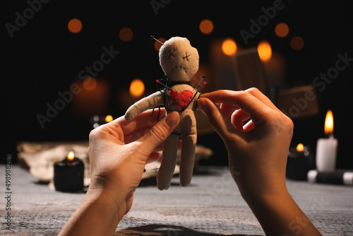 Woman stabbing voodoo doll with pin at wooden table indoors, closeup photo