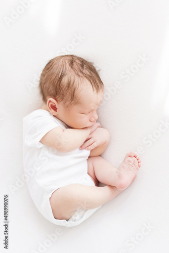 newborn baby in fetal position sleeps cute on white blanket in white bodysuit