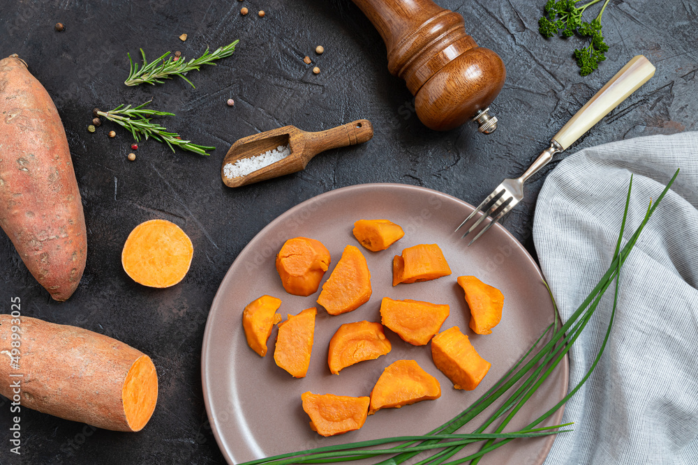 Baked sweet potatoes, raw yam and spices on a dark table - plant-based eating, top view Baked sweet potatoes, raw yam and spices on a dark table - plant-based eating, top view