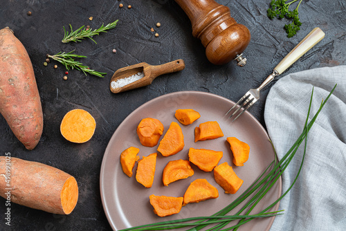 Baked sweet potatoes, raw yam and spices on a dark table - plant-based eating, top view