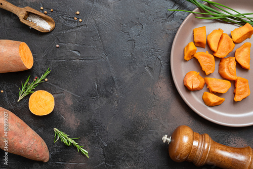 Roasted sweet potatoes, raw yam and spices on a dark table - vegetarian healthy food, top view with copy space
