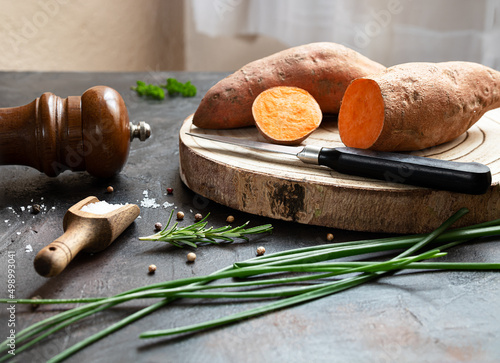 Raw organic yam - sweet potatoes on a cutting board and spices on a dark table