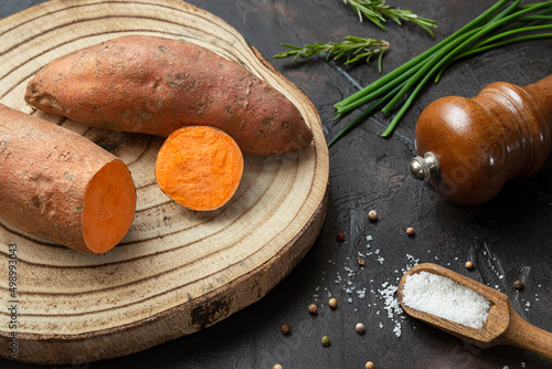 Raw sweet potatoes, organic yam on a cutting board and spices on a dark table, top view
