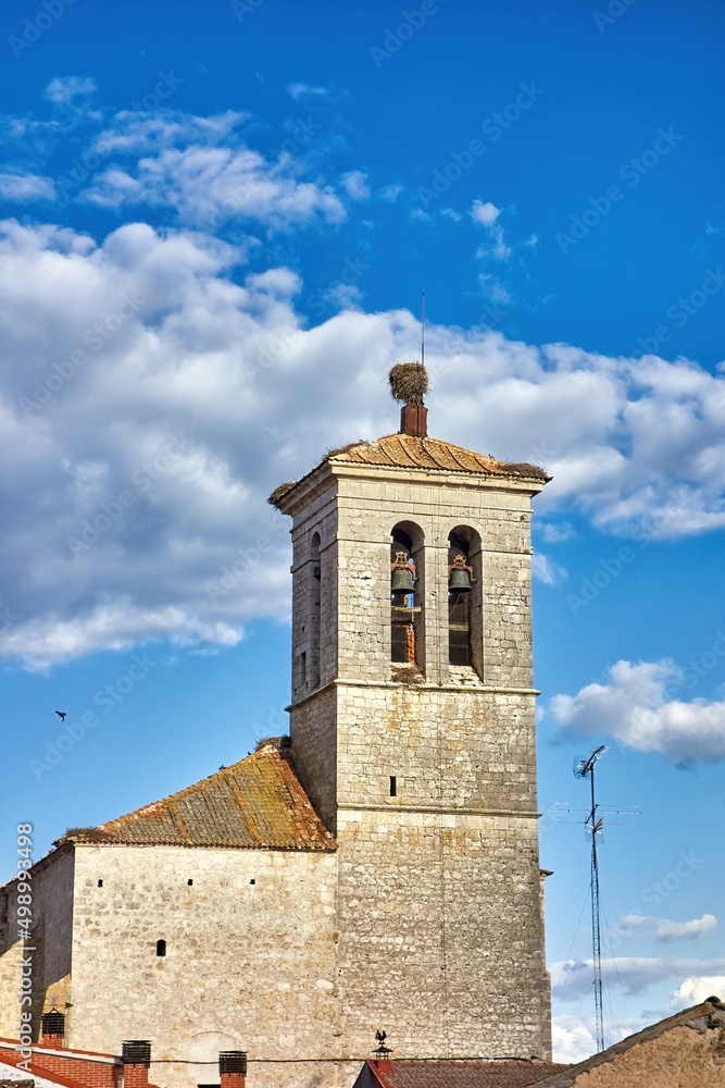 Detail of the bell tower of a rural church with stork nests on its roof and a nice blue cloudy sky behind              