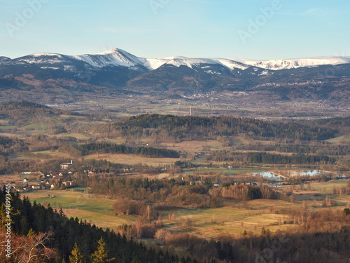 The spring landscape of Rudawy Janowickie at sunrise with the snow-covered Karkonosze Mountains in the background. Horizontal view from the top Sokolik Big on forests, fields and mountains.