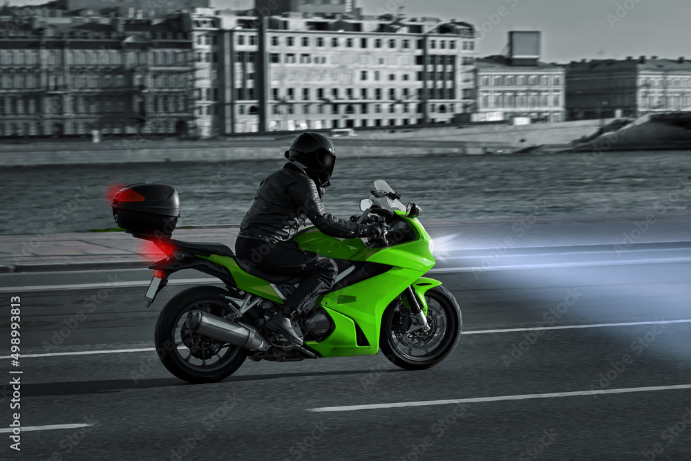 A woman rides a motorcycle in the night city. Motorcyclist rides along the embankment on a green sports bike. Motorcycle travel. Headlights at night.