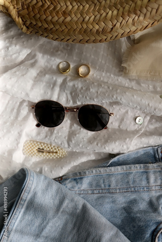 Mom jeans, white blouse, boho scarf, wicker bag, sunglasses, gold rings and pearl accessories. Flat lay.