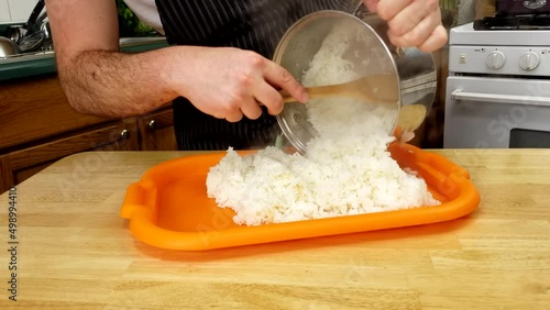 Home cooking - Transferring cooked short grain white rice onto plastic orange tray to be seasoned with vinegar and sugar in preparation for sushi.