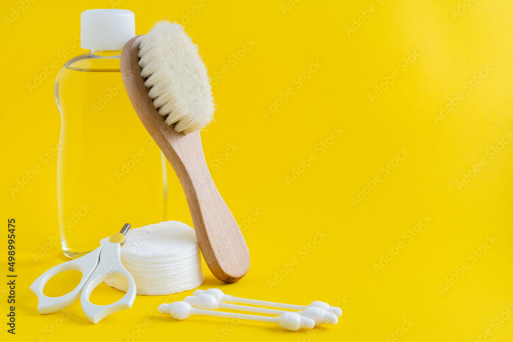 Scissors, wooden hair brush, bottle of baby cosmetics, cotton pads and cotton ear sticks on yellow background. Composition of products for baby care. Image for sites about babies and products for baby Scissors, wooden hair brush, bottle of baby cosmetics, cotton pads and cotton ear sticks on yellow background. Composition of products for baby care. Image for sites about babies and products for baby