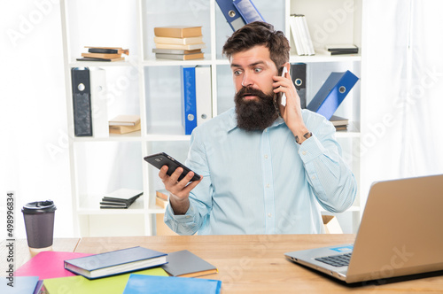Shocked businessman talking on cellphone using smartphone at office desk, mobility