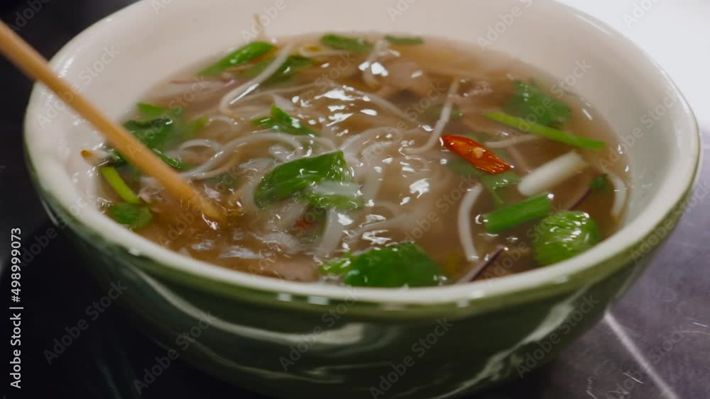 Stirs Vietnamese soup with chopsticks. Fragrant beef broth with the addition of Vietnamese spices and herbs, cooked according to all the traditions of ancient Hanoi, with the addition of rice fo Stirs Vietnamese soup with chopsticks. Fragrant beef broth with the addition of Vietnamese spices and herbs, cooked according to all the traditions of ancient Hanoi, with the addition of rice fo