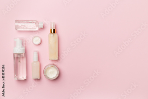 Different cosmetic bottles and container on color background, top view