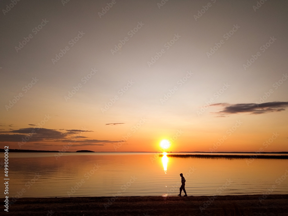 Sunset over the lake. The guy walks against the background of sunrise over the sea