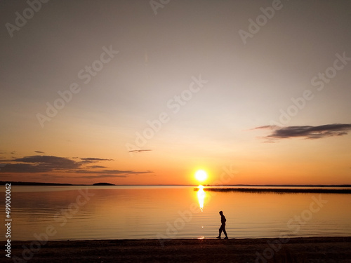 Sunset over the lake. The guy walks against the background of sunrise over the sea
