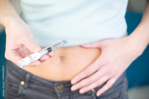 Close-up of a woman's hands and stomach giving herself an insulin.