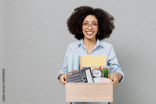 Young smiling optimistic employee business corporate lawyer woman of African American ethnicity in classic formal shirt work in office hold cardboard box with stuff isolated on grey background studio. photo