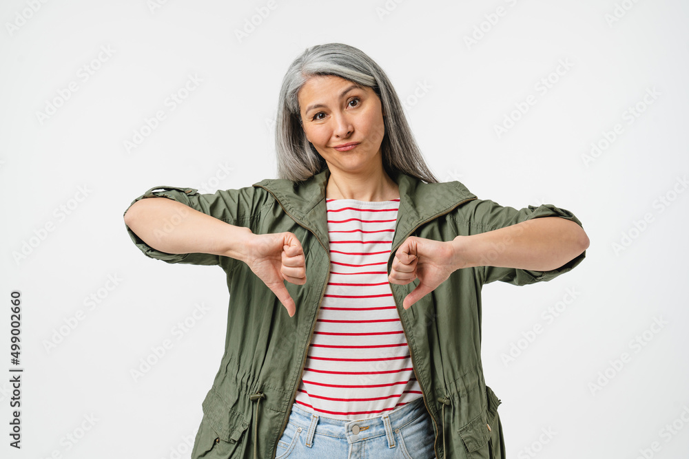 Sad disappointed mature middle-aged caucasian woman with grey hair showing thumbs down for disagreement isolated in white background. Negative attitude Sad disappointed mature middle-aged caucasian woman with grey hair showing thumbs down for disagreement isolated in white background. Negative attitude