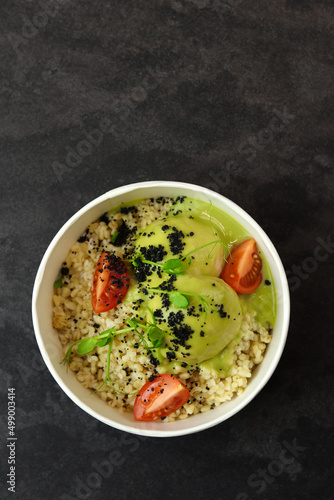 Bowl with bulgur, tomatoes, chicken meatballs and broccoli sauce in eco paper container on black background. Healthy food delivery service and daily ration concept.