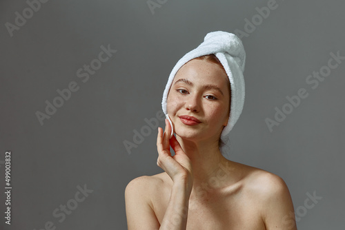 Pretty young girl in towel do skincare routine cleansing skin by cotton pad, micellar water. Self-care, personal hygiene
